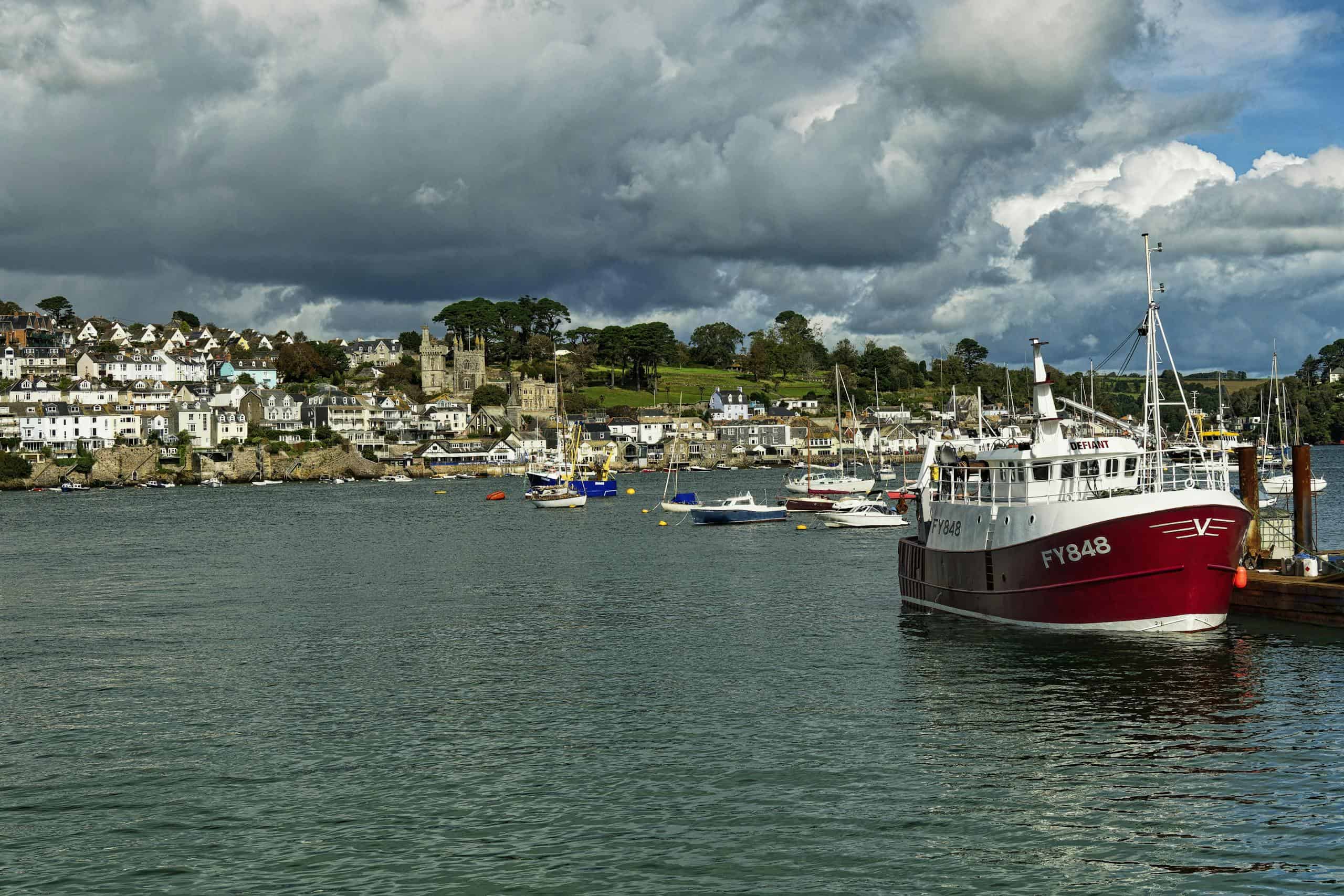 Charming coastal village harbor with boats under dramatic clouds.
